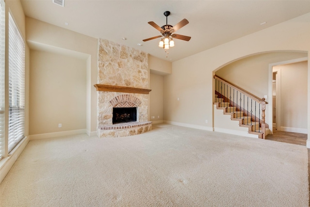 unfurnished living room with a stone fireplace, ceiling fan, and light carpet