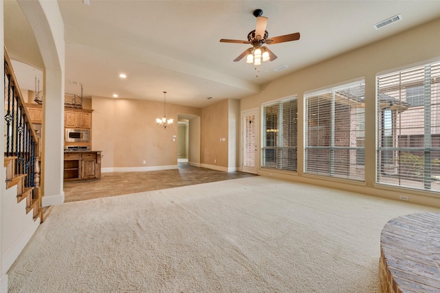 unfurnished living room featuring ceiling fan with notable chandelier and light colored carpet