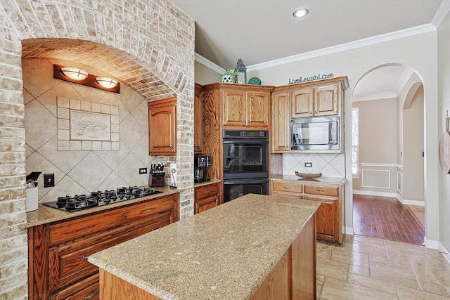 kitchen with light stone counters, stainless steel microwave, gas stovetop, double oven, and ornamental molding