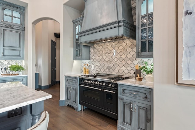 kitchen featuring dark wood-type flooring, light stone countertops, double oven range, custom range hood, and backsplash