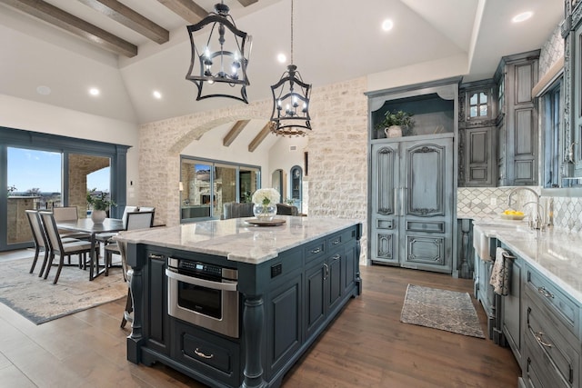 kitchen with a center island, stainless steel oven, light stone countertops, beam ceiling, and decorative light fixtures