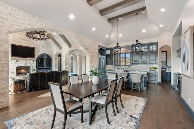 dining area with dark wood-type flooring, high vaulted ceiling, beamed ceiling, and a stone fireplace