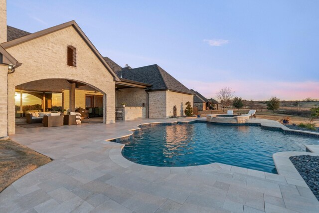 pool at dusk featuring a patio area, an in ground hot tub, and an outdoor living space