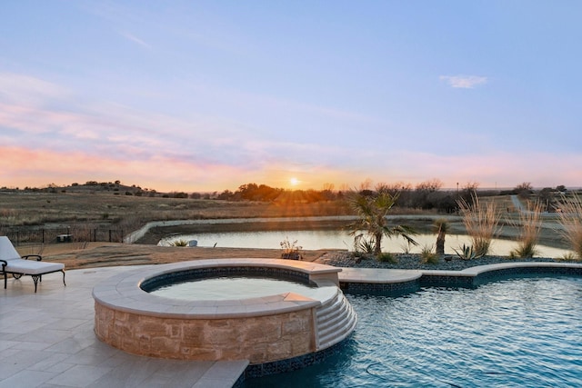 pool at dusk with a patio area, an in ground hot tub, and a water view