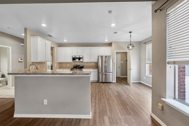 kitchen featuring pendant lighting, appliances with stainless steel finishes, white cabinetry, light stone countertops, and kitchen peninsula