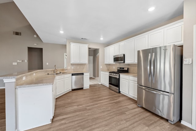 kitchen with sink, white cabinetry, stainless steel appliances, light stone countertops, and kitchen peninsula