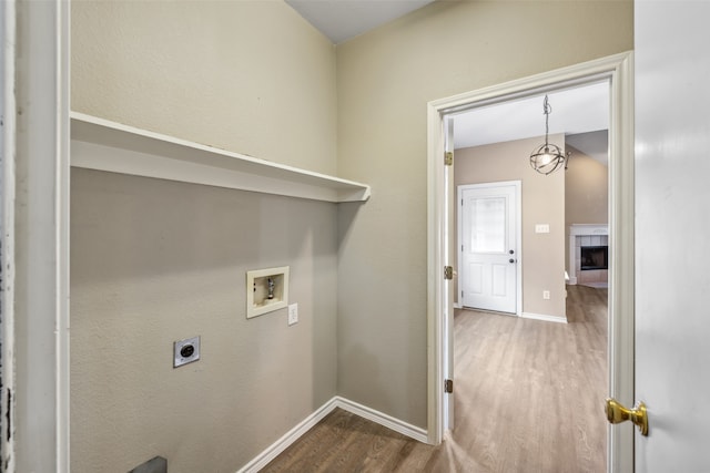 laundry room featuring electric dryer hookup, hookup for a washing machine, a tiled fireplace, and hardwood / wood-style flooring