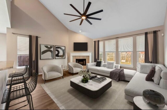 living room featuring light wood-type flooring, high vaulted ceiling, ceiling fan, and a tiled fireplace