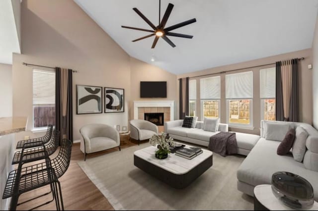 living room with ceiling fan, high vaulted ceiling, a tile fireplace, and light hardwood / wood-style flooring