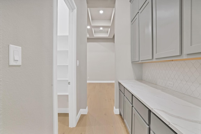 interior space with gray cabinets, light stone counters, a tray ceiling, and light hardwood / wood-style floors