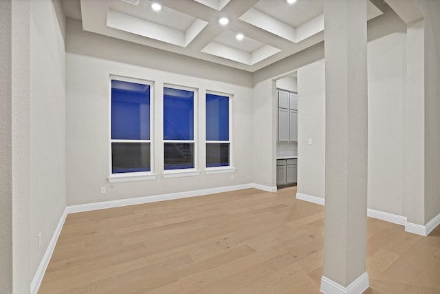 empty room with beam ceiling, coffered ceiling, and light wood-type flooring