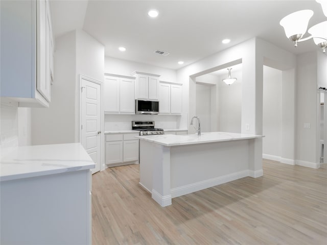 kitchen with decorative light fixtures, white cabinets, light hardwood / wood-style floors, light stone counters, and stainless steel appliances