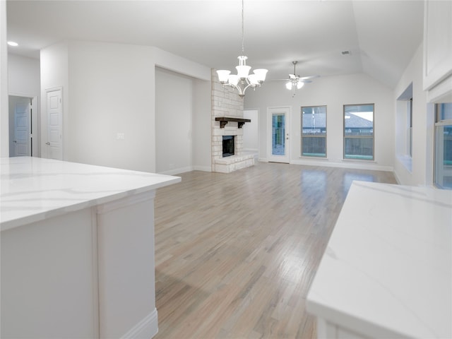 unfurnished living room with light hardwood / wood-style flooring, ceiling fan with notable chandelier, a fireplace, and vaulted ceiling