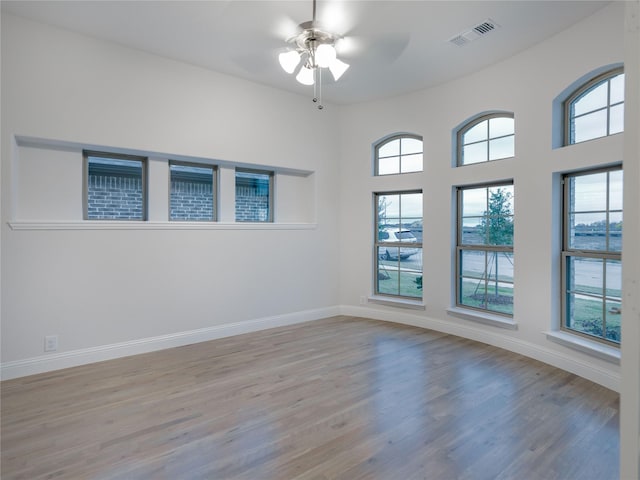 empty room with a wealth of natural light, light wood-type flooring, and ceiling fan