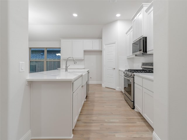 kitchen featuring stainless steel appliances, white cabinetry, light stone countertops, and light wood-type flooring