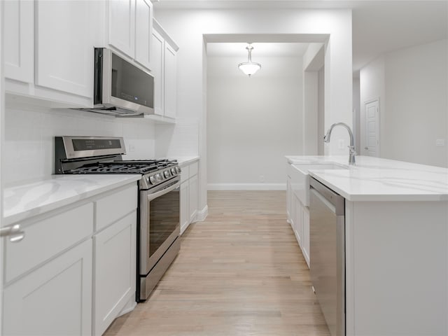 kitchen with appliances with stainless steel finishes, tasteful backsplash, white cabinetry, light stone countertops, and a center island with sink