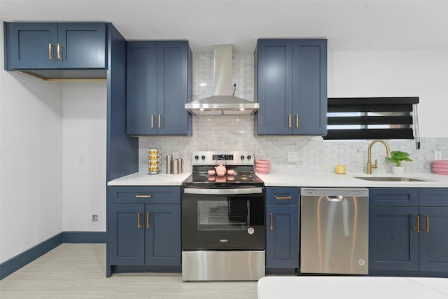 kitchen featuring stainless steel appliances, a sink, wall chimney range hood, blue cabinetry, and tasteful backsplash