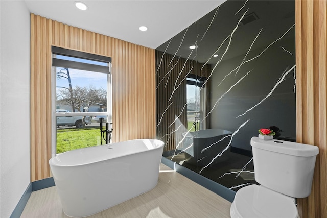 bathroom with a tub to relax in and toilet