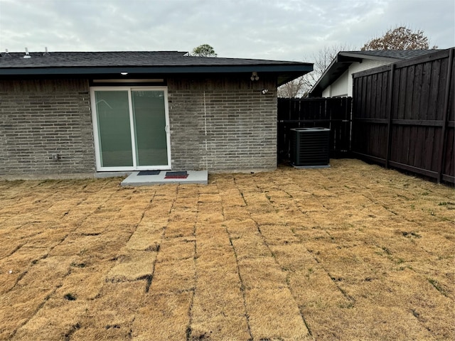 back of house featuring brick siding, roof with shingles, cooling unit, and fence