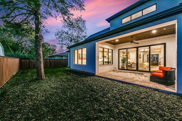 back house at dusk featuring a lawn, a patio, and ceiling fan