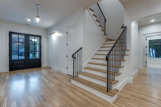 foyer entrance with french doors, crown molding, and light hardwood / wood-style flooring