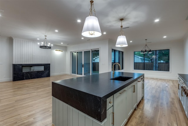 kitchen with pendant lighting, sink, white cabinetry, and a center island with sink