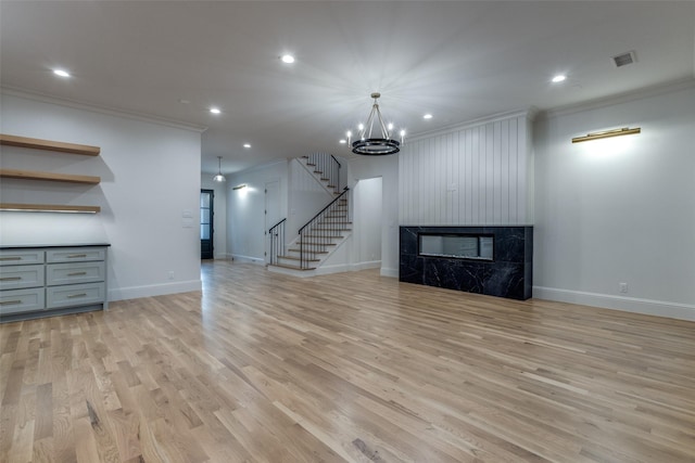 unfurnished living room with ornamental molding, a chandelier, a fireplace, and light hardwood / wood-style floors