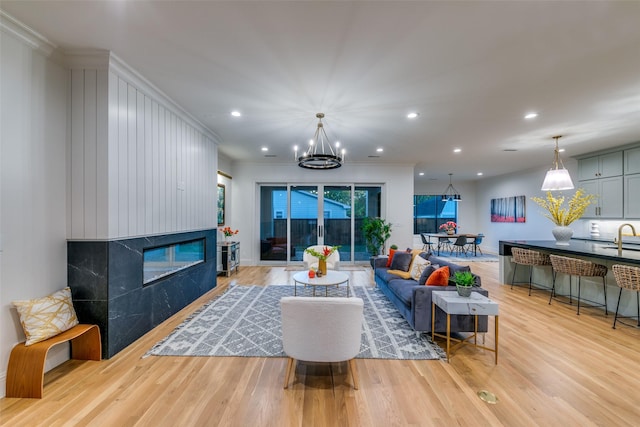 living room featuring sink, crown molding, a fireplace, a notable chandelier, and light hardwood / wood-style floors