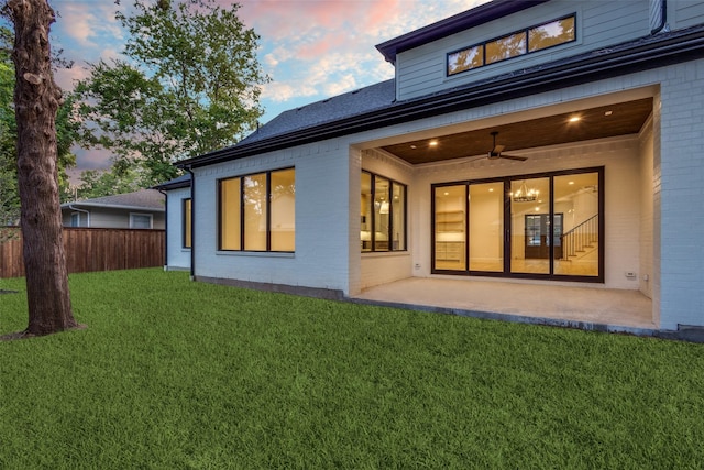 back house at dusk featuring ceiling fan, a yard, and a patio