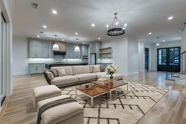 living room with sink, crown molding, a notable chandelier, and light wood-type flooring