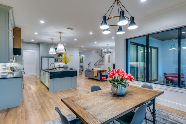 dining room with sink, an inviting chandelier, ornamental molding, and light wood-type flooring