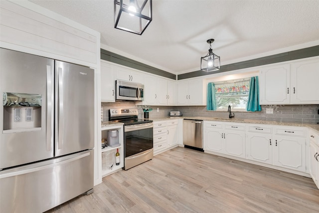 kitchen with appliances with stainless steel finishes, a sink, white cabinetry, and light wood-style floors