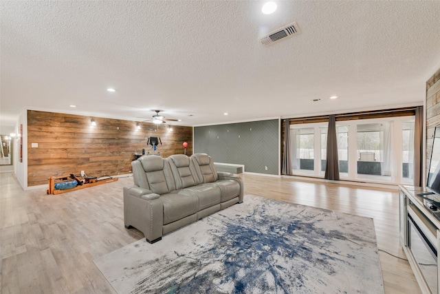 living room with ceiling fan, a textured ceiling, wood walls, and light wood-type flooring