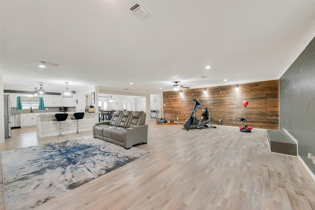 living room featuring ceiling fan, wood walls, a textured ceiling, and light hardwood / wood-style floors