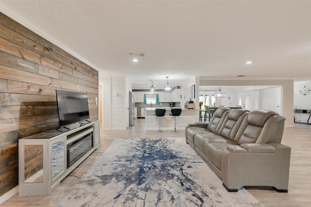 living room with a textured ceiling, an inviting chandelier, light hardwood / wood-style flooring, and wooden walls