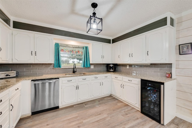 kitchen with sink, beverage cooler, pendant lighting, stainless steel dishwasher, and white cabinets