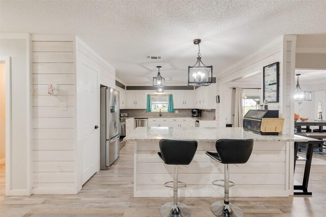 kitchen with light stone countertops, stainless steel appliances, light wood-style floors, a kitchen bar, and white cabinetry