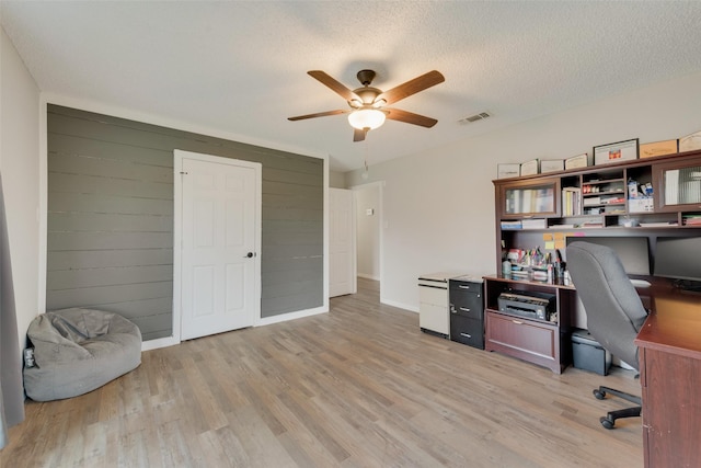 office area featuring a textured ceiling, ceiling fan, wooden walls, and light hardwood / wood-style floors