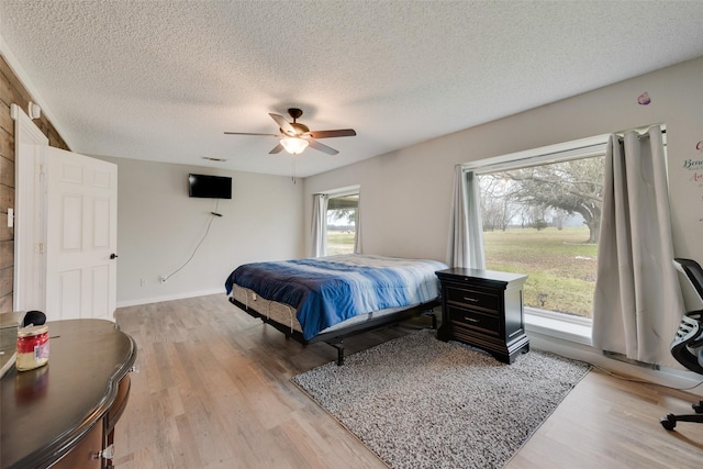 bedroom with ceiling fan, light hardwood / wood-style flooring, and a textured ceiling