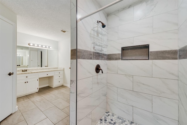 bathroom featuring tiled shower, vanity, and a textured ceiling