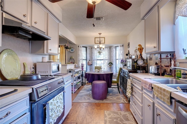 kitchen with white microwave, under cabinet range hood, stove, light countertops, and hanging light fixtures