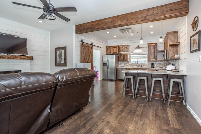 living room featuring wood walls, beamed ceiling, dark hardwood / wood-style flooring, ceiling fan, and a barn door