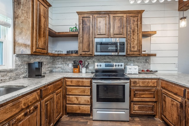 kitchen with wooden walls, dark hardwood / wood-style floors, stainless steel appliances, light stone countertops, and decorative backsplash