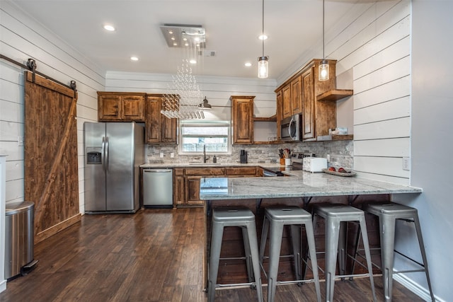 kitchen with sink, stainless steel appliances, light stone counters, a barn door, and kitchen peninsula