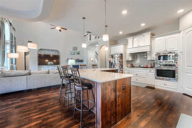 kitchen with a kitchen island with sink, appliances with stainless steel finishes, a breakfast bar, decorative backsplash, and white cabinetry