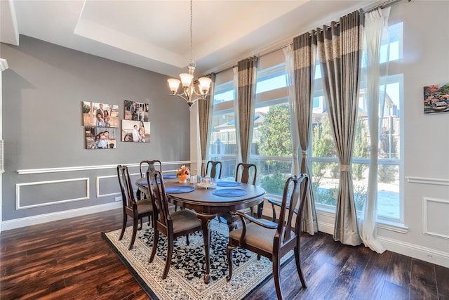 dining room featuring dark hardwood / wood-style flooring, a wealth of natural light, a tray ceiling, and a notable chandelier