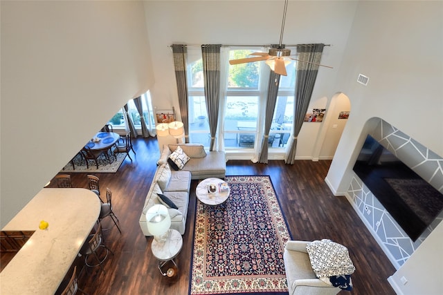 living room featuring a towering ceiling, ceiling fan, and dark wood-type flooring