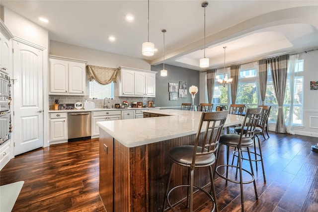 kitchen with a raised ceiling, hanging light fixtures, dark hardwood / wood-style floors, white cabinetry, and stainless steel dishwasher