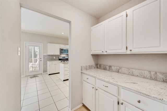 kitchen with light tile patterned floors, appliances with stainless steel finishes, white cabinets, light stone countertops, and backsplash