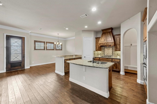 kitchen featuring premium range hood, dark hardwood / wood-style floors, an island with sink, pendant lighting, and stainless steel gas stovetop